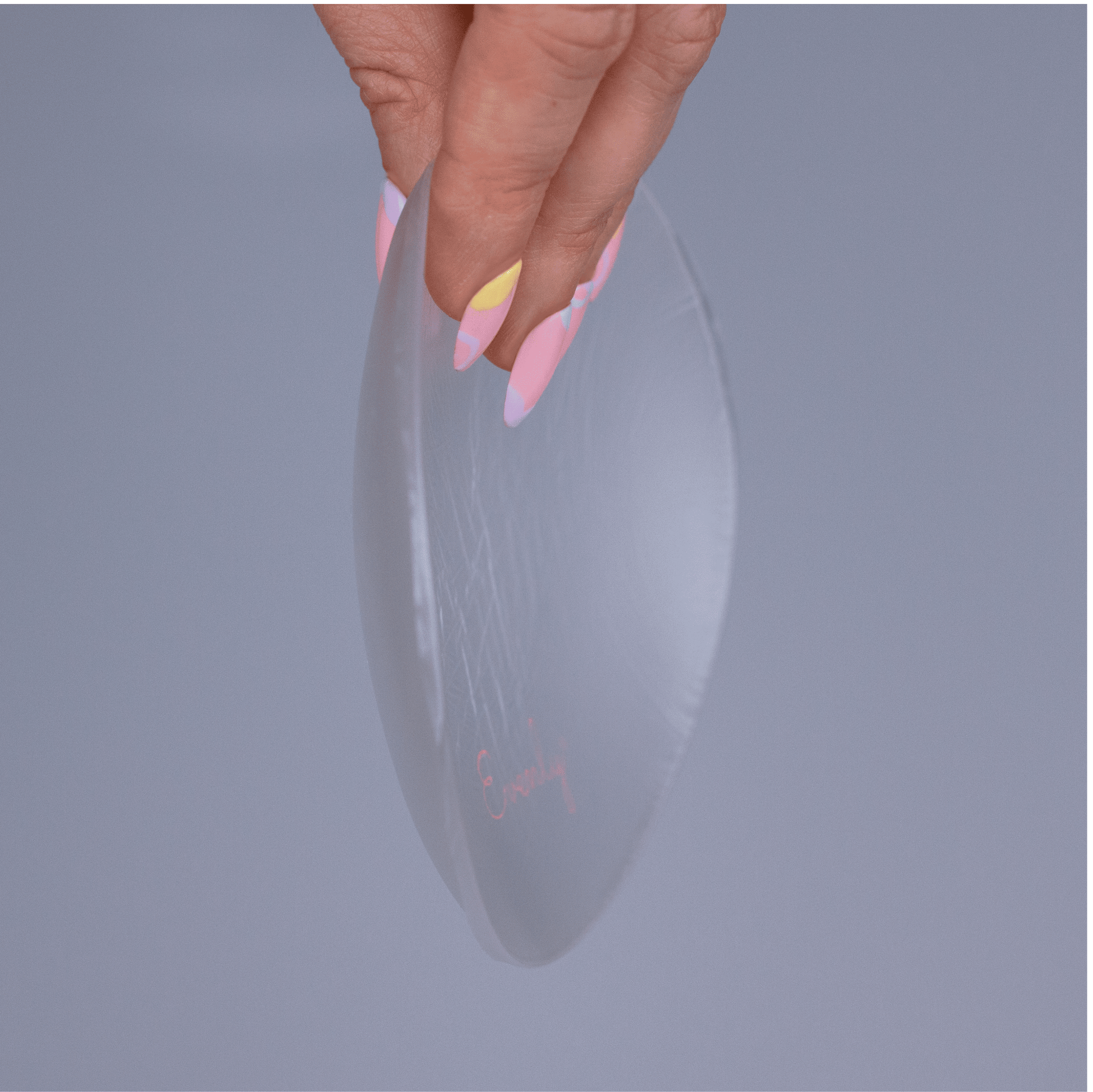 Hand holding a clear silicone bra balancer against a gray background
