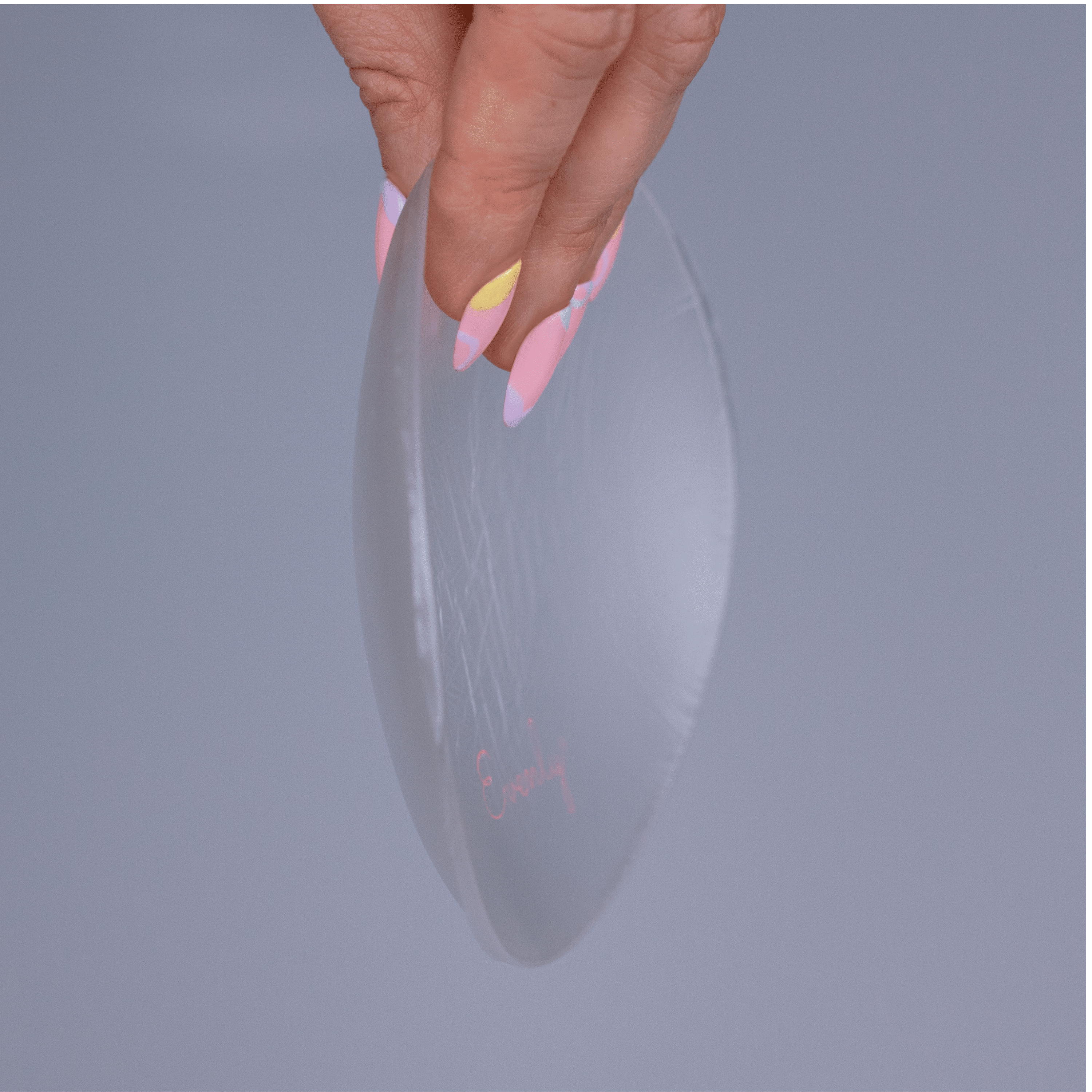 Hand holding a clear silicone bra balancer against a gray background